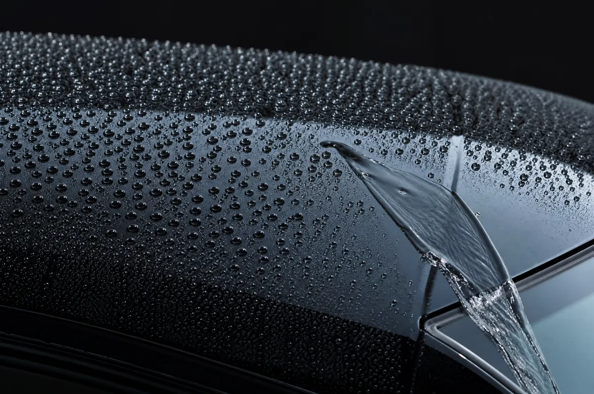Tight water beads standing on a coated black hood with a strip of water sheeting off