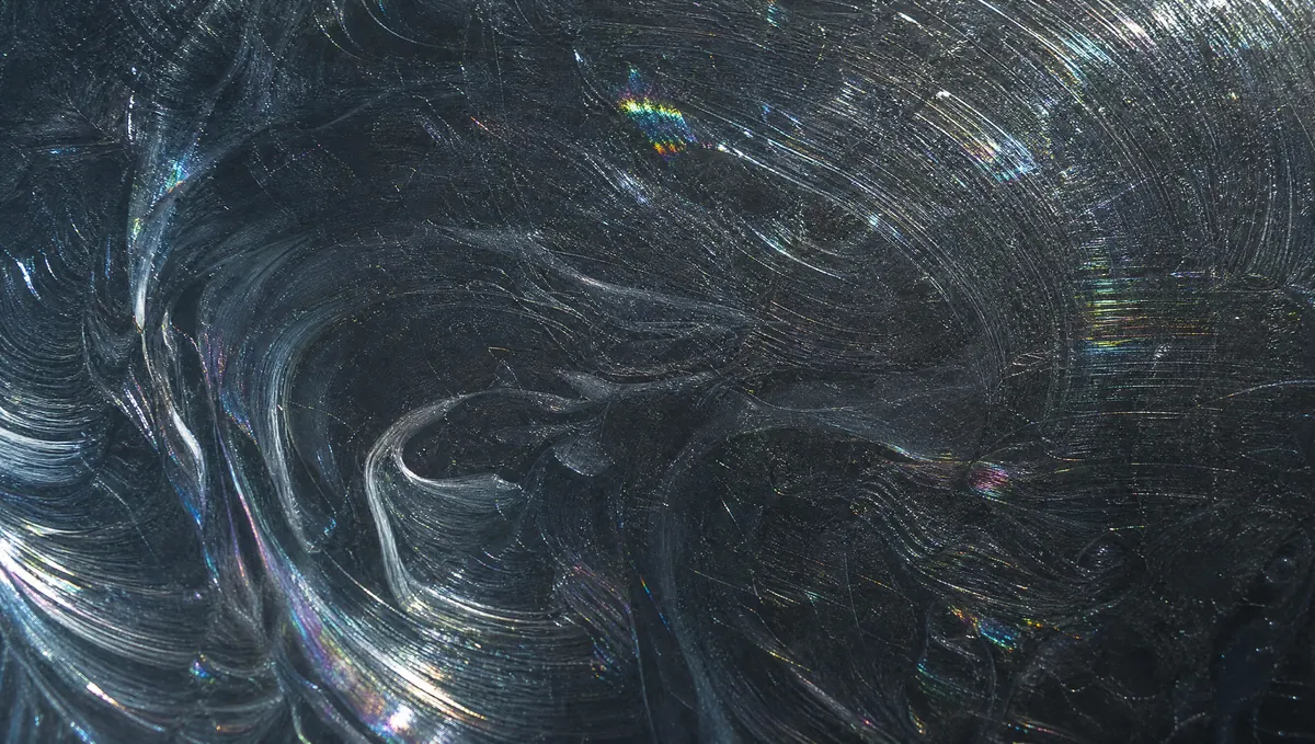 A macro view of swirl marks on black paint, a web of fine circular scratches catching the light