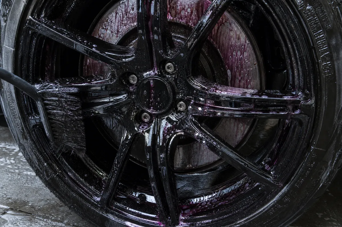 A black alloy wheel streaked purple as iron remover reacts with brake dust, water sheeting off the spokes